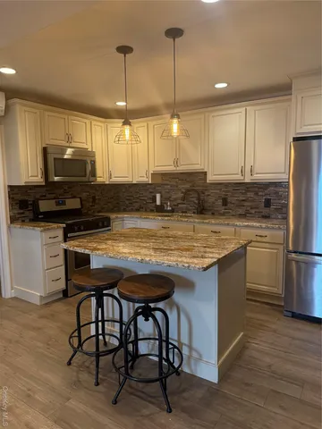 a kitchen with kitchen island a stove a sink a refrigerator wooden floor dining table and chairs