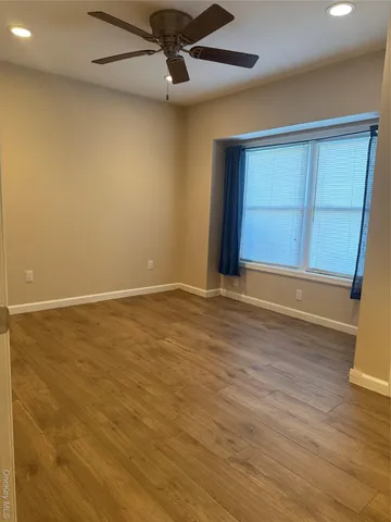 an empty room with wooden floor fan and windows