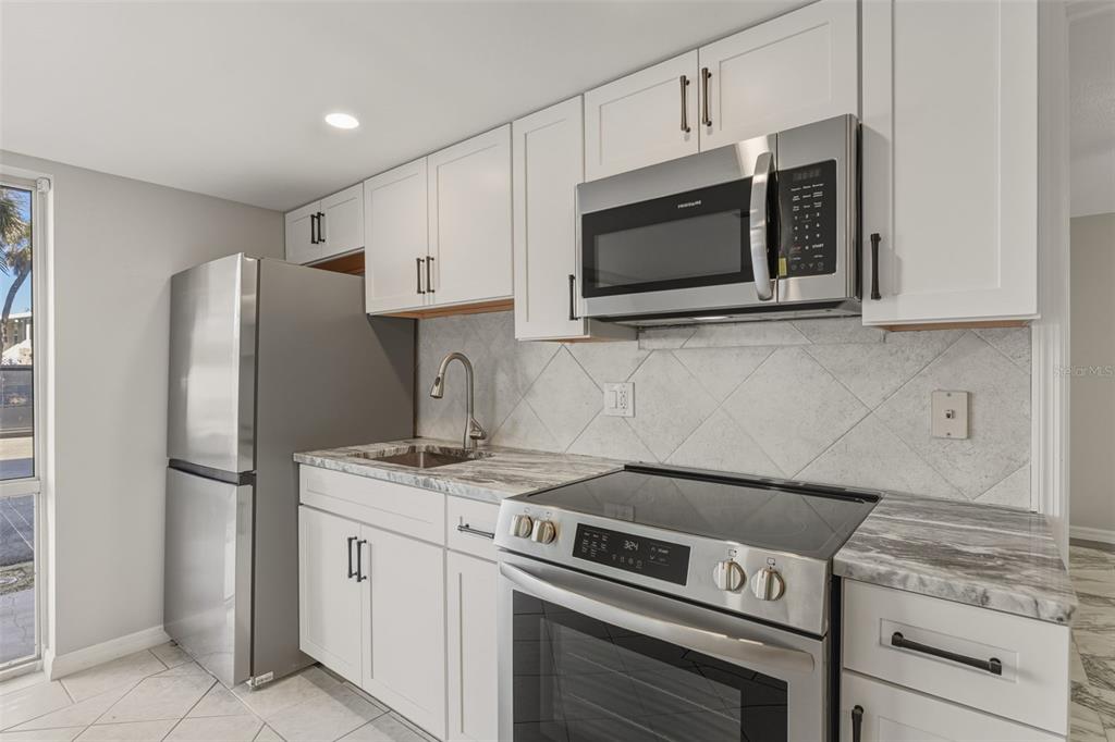 5055 North Beach Road, Unit 106 Englewood, FL 34223 - Photo 7 of 34 a kitchen with stainless steel appliances granite countertop white cabinets a microwave a sink and a refrigerator