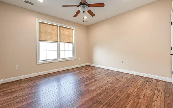 an empty room with wooden floor chandelier fan and windows