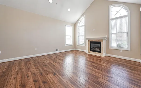 an empty room with wooden floor fireplace and windows