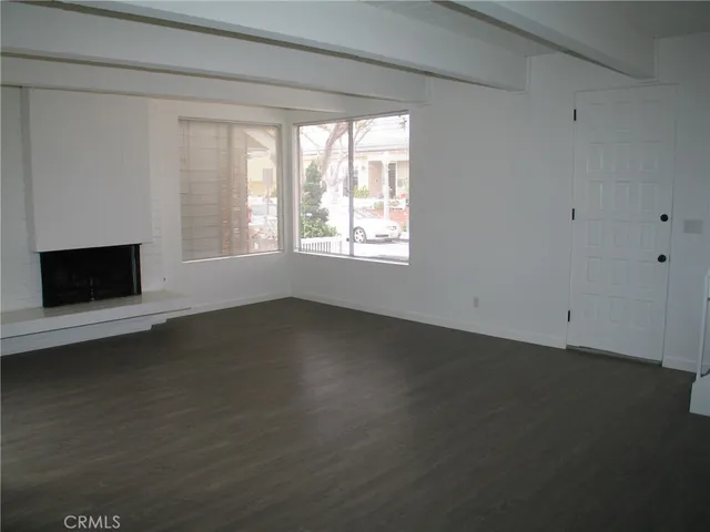 an empty room with wooden floor fireplace and windows