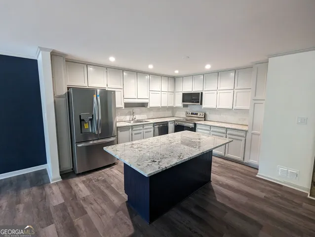 a kitchen with kitchen island a refrigerator a stove a sink and white cabinets with wooden floor