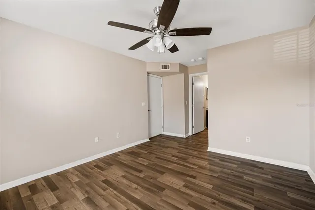 an empty room with wooden floor fan and windows
