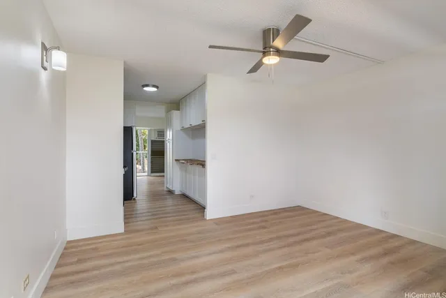 a view of an empty room with wooden floor and a ceiling fan