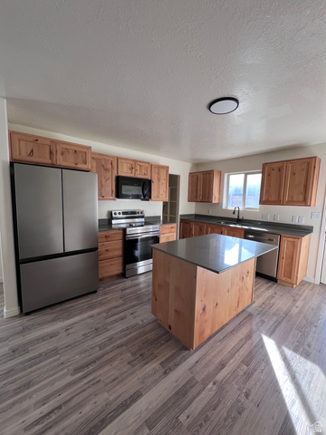 1696 South Longview Road Santaquin, UT 84655 - Photo 3 of 16 Kitchen with stainless steel appliances, dark countertops, a kitchen island, a textured ceiling, and dark wood-type flooring