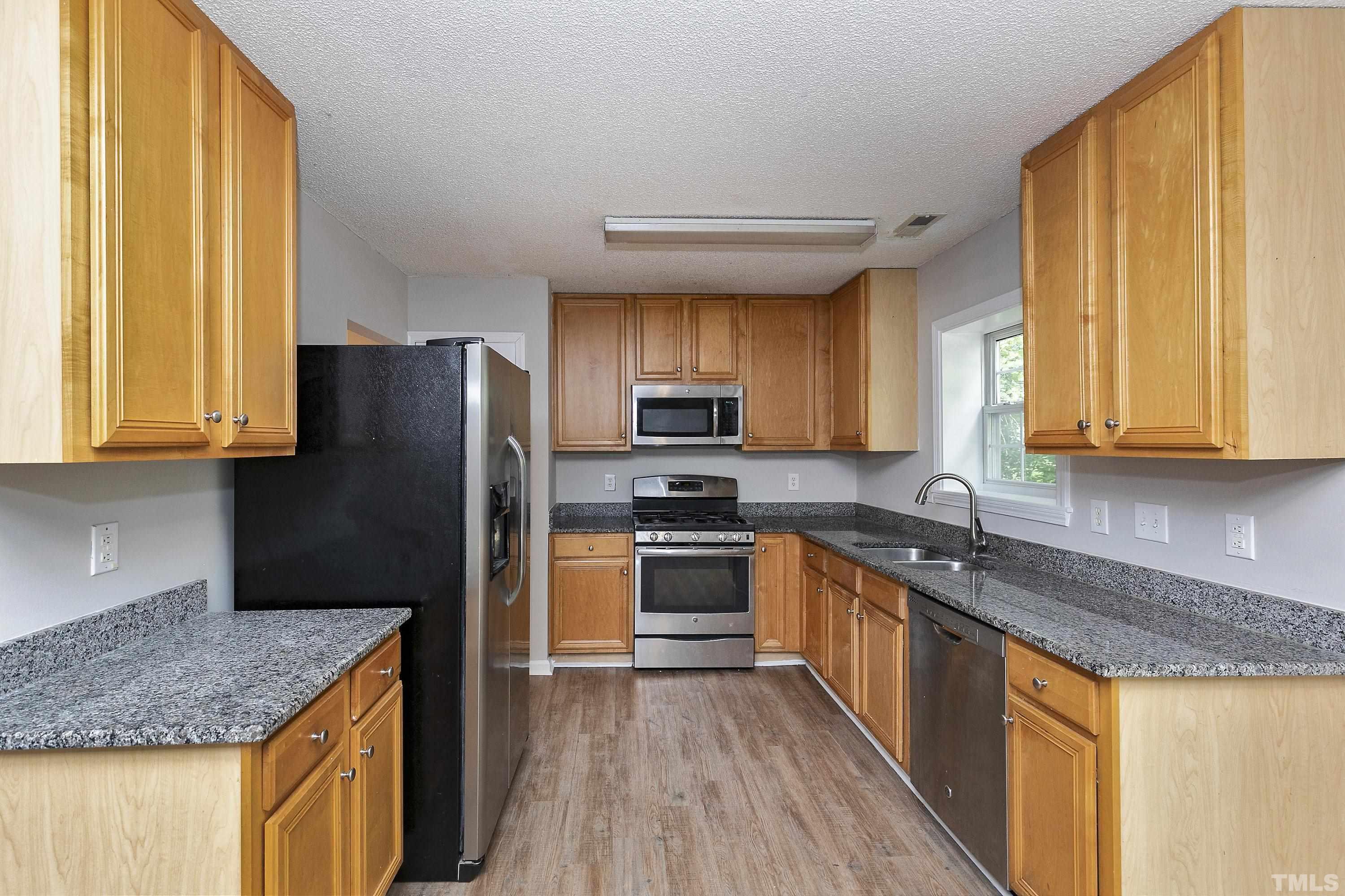 613 Branchview Drive Durham, NC 27713 - Photo 7 of 40 a kitchen with granite countertop wooden cabinets a sink a window and stainless steel appliances