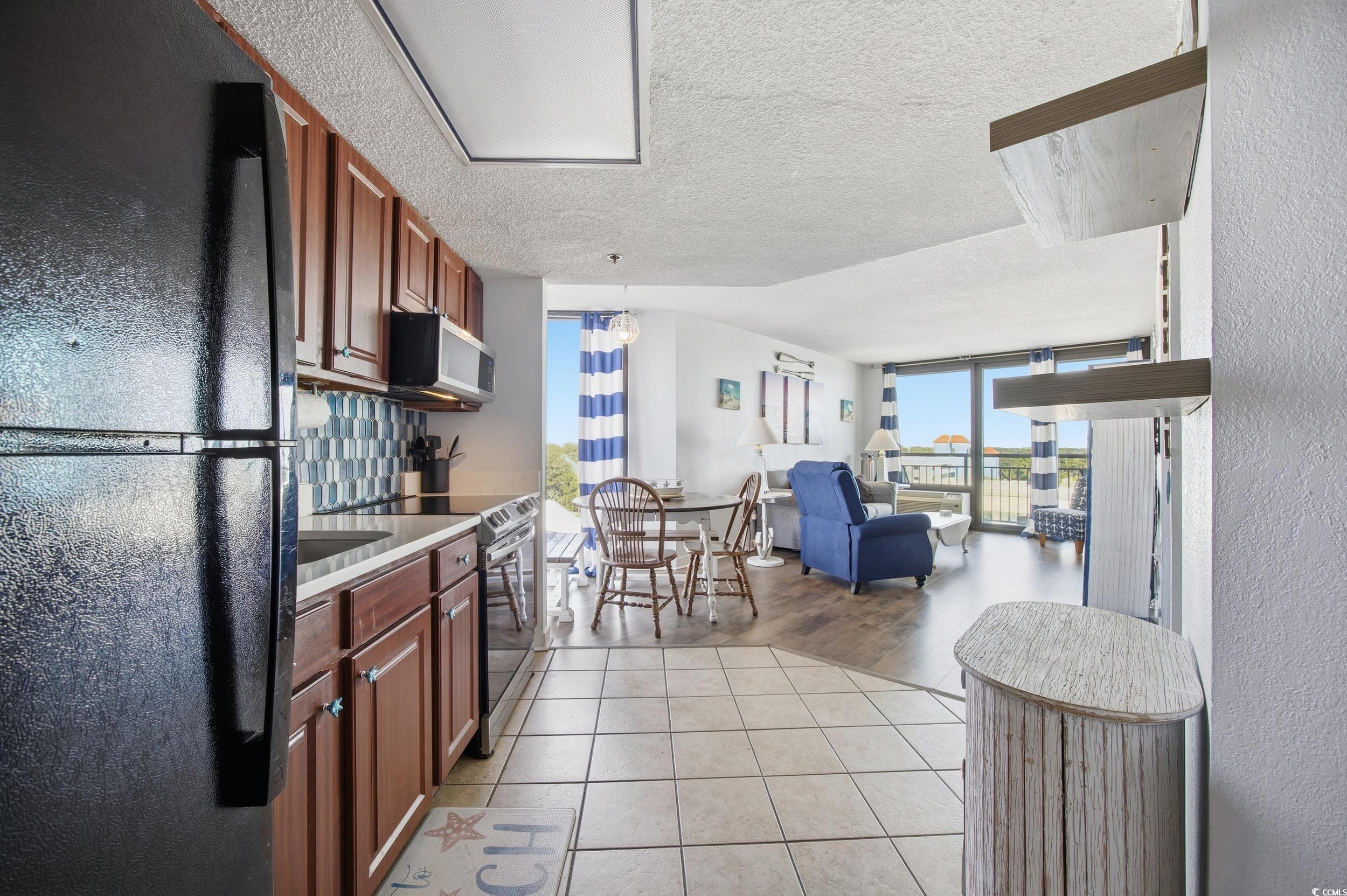 2710 North Ocean Boulevard, Unit 702 Myrtle Beach, SC 29577 - Photo 37 of 38 Kitchen with appliances with stainless steel finishes, a textured ceiling, light tile patterned floors, open floor plan, and tasteful backsplash