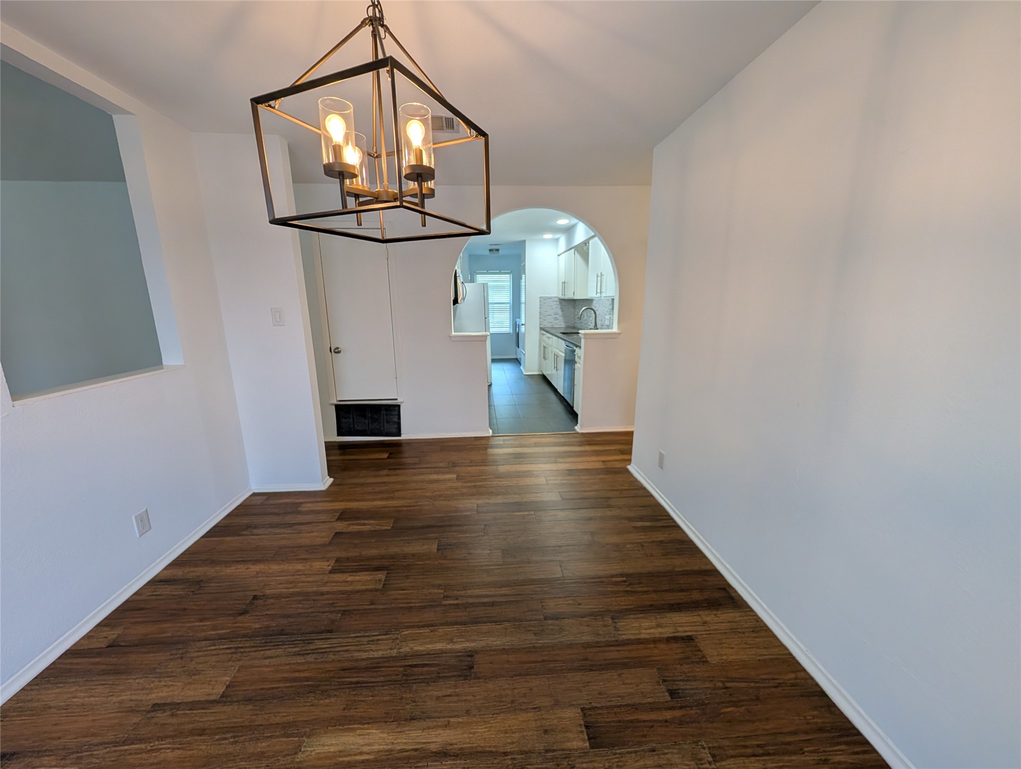 4601 Tamarack Trail Austin, TX 78727 - Photo 5 of 19 An open dining area with rich wood flooring flows into an arched kitchen entry, illuminated by a contemporary chandelier.