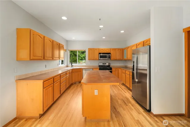 a large kitchen with stainless steel appliances granite countertop a refrigerator a sink dishwasher a stove and white countertops with wooden floor