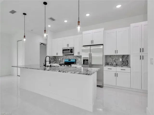 a kitchen with stainless steel appliances granite countertop a refrigerator a sink a stove and white cabinets