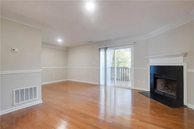 a view of an empty room with wooden floor fireplace and a window