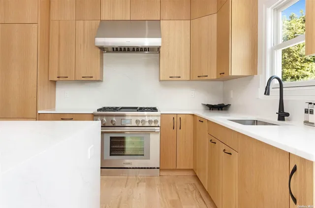 a kitchen with stainless steel appliances granite countertop a stove a sink and white cabinets with wooden floor