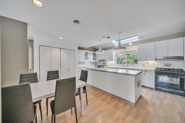a kitchen with stainless steel appliances granite countertop a stove top oven a sink dishwasher a refrigerator and white cabinets with wooden floor