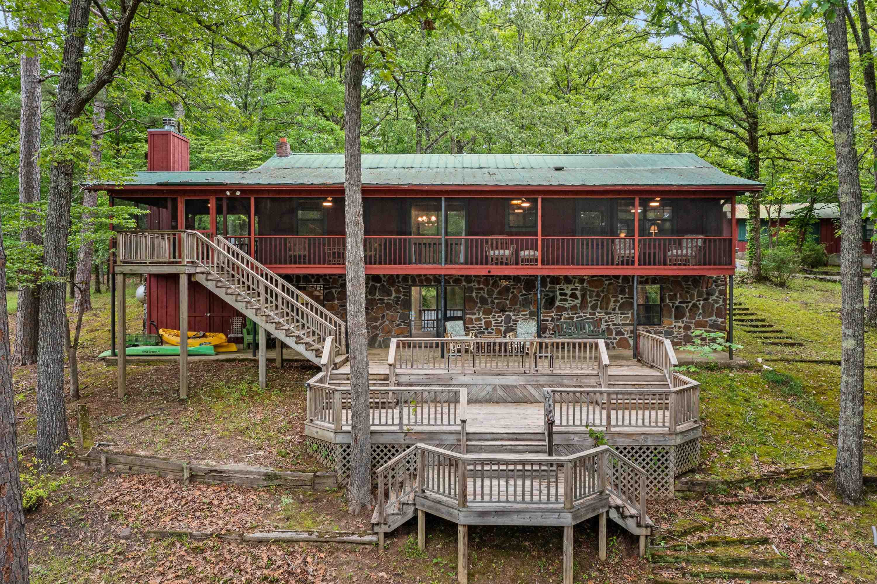 Rear view of property with stairway, a chimney, a sunroom, a wooden deck, and stone siding