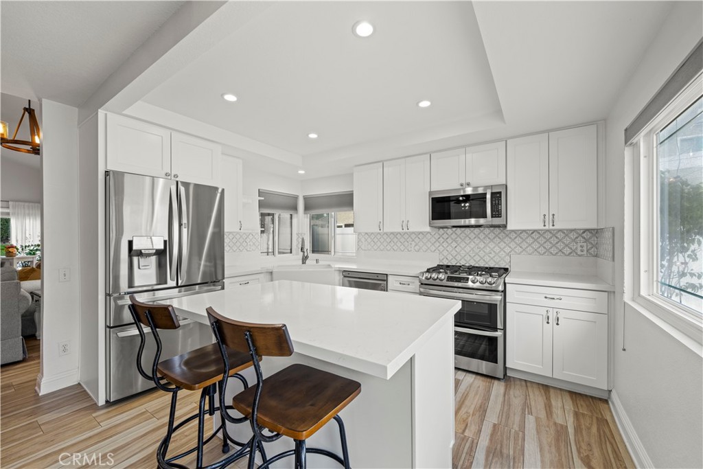 a kitchen with stainless steel appliances a stove a sink dishwasher a refrigerator white cabinets and wooden floor