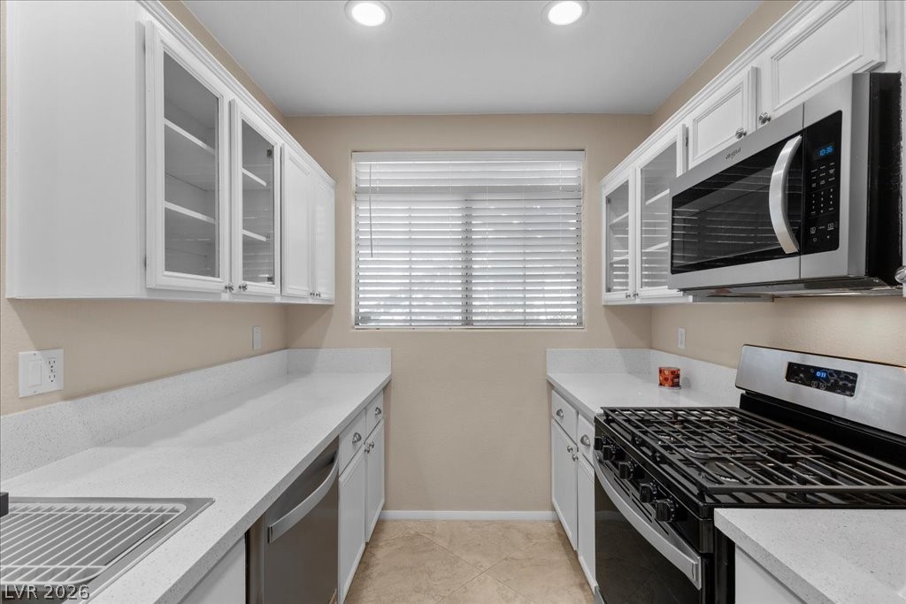 Kitchen featuring glass insert cabinets, stainless steel appliances, white cabinets, light stone counters, and recessed lighting