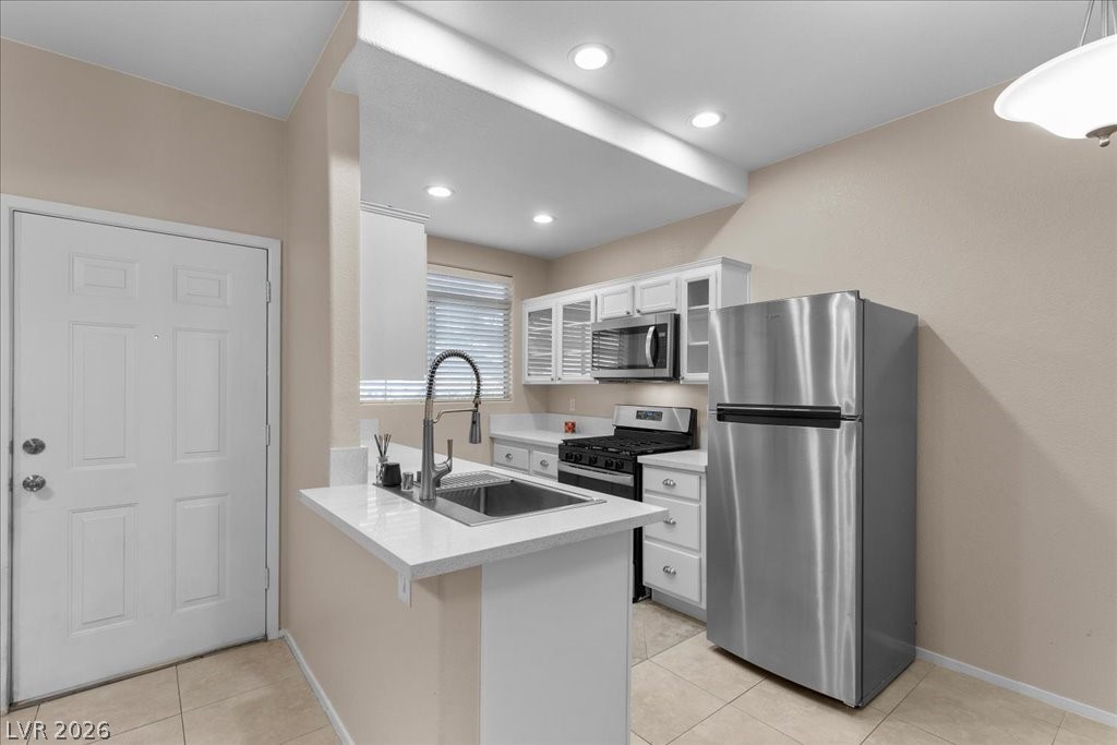 2201 Ramsgate Drive, Unit 818 Henderson, NV 89074 - Photo 4 of 31 Kitchen with stainless steel appliances, a peninsula, white cabinets, glass insert cabinets, and light tile patterned floors