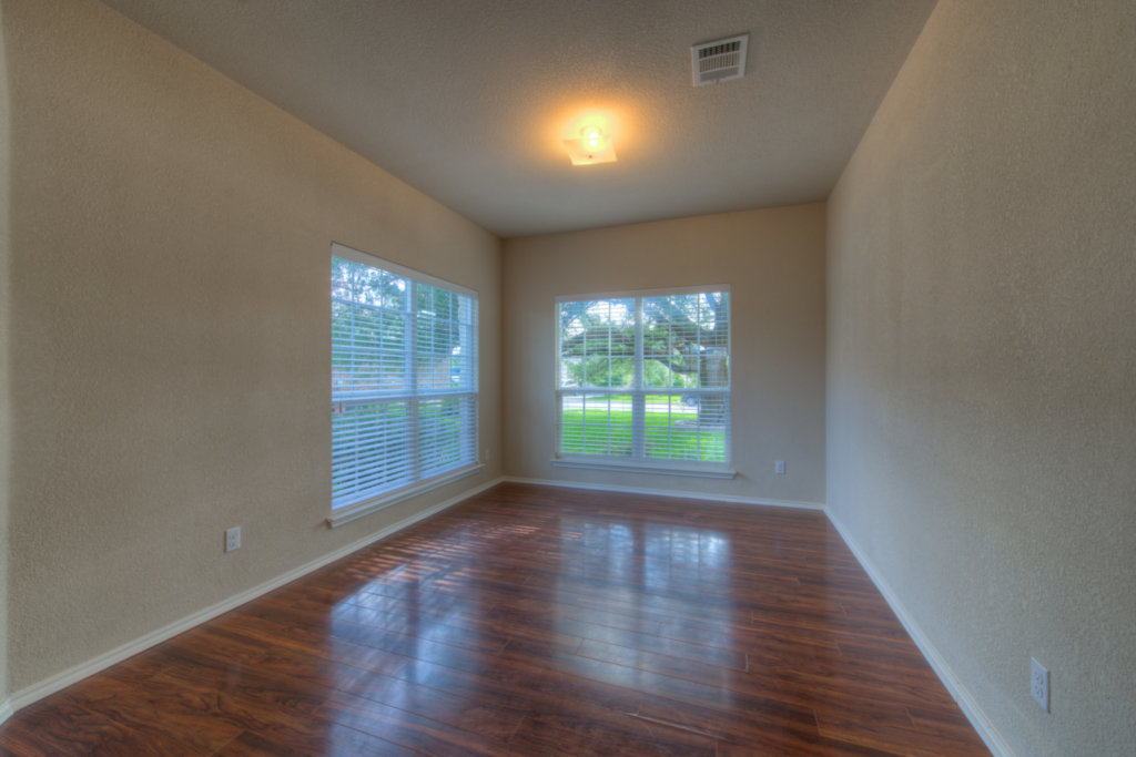 Gleaming hardwood floors run throughout this versatile empty room illuminated by two large windows.