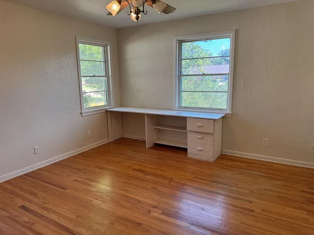 an empty room with wooden floor cabinet and windows