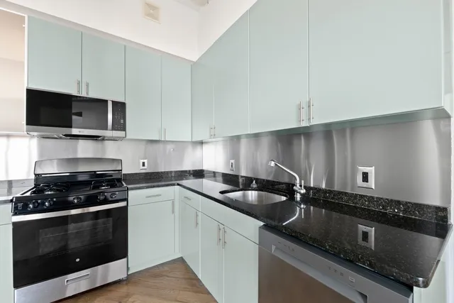 a kitchen with stainless steel appliances granite countertop a stove a refrigerator a sink dishwasher and a dining table with wooden floor