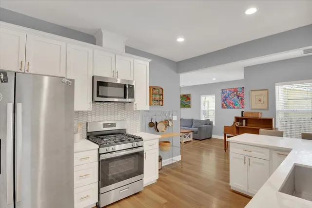 a kitchen with stainless steel appliances a stove a refrigerator a sink a stove oven and white cabinets with wooden floor