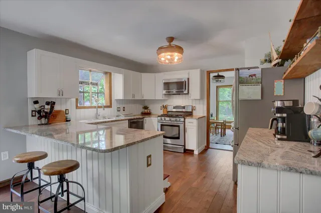 a kitchen with stainless steel appliances granite countertop a stove top oven a sink dishwasher a dining table and chairs with wooden floor