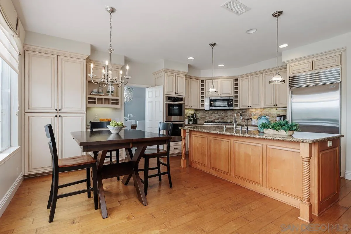 6943 Wildrose Terrace Carlsbad, CA 92011 - Photo 11 of 34 a kitchen with stainless steel appliances kitchen island granite countertop a dining table chairs and white cabinets