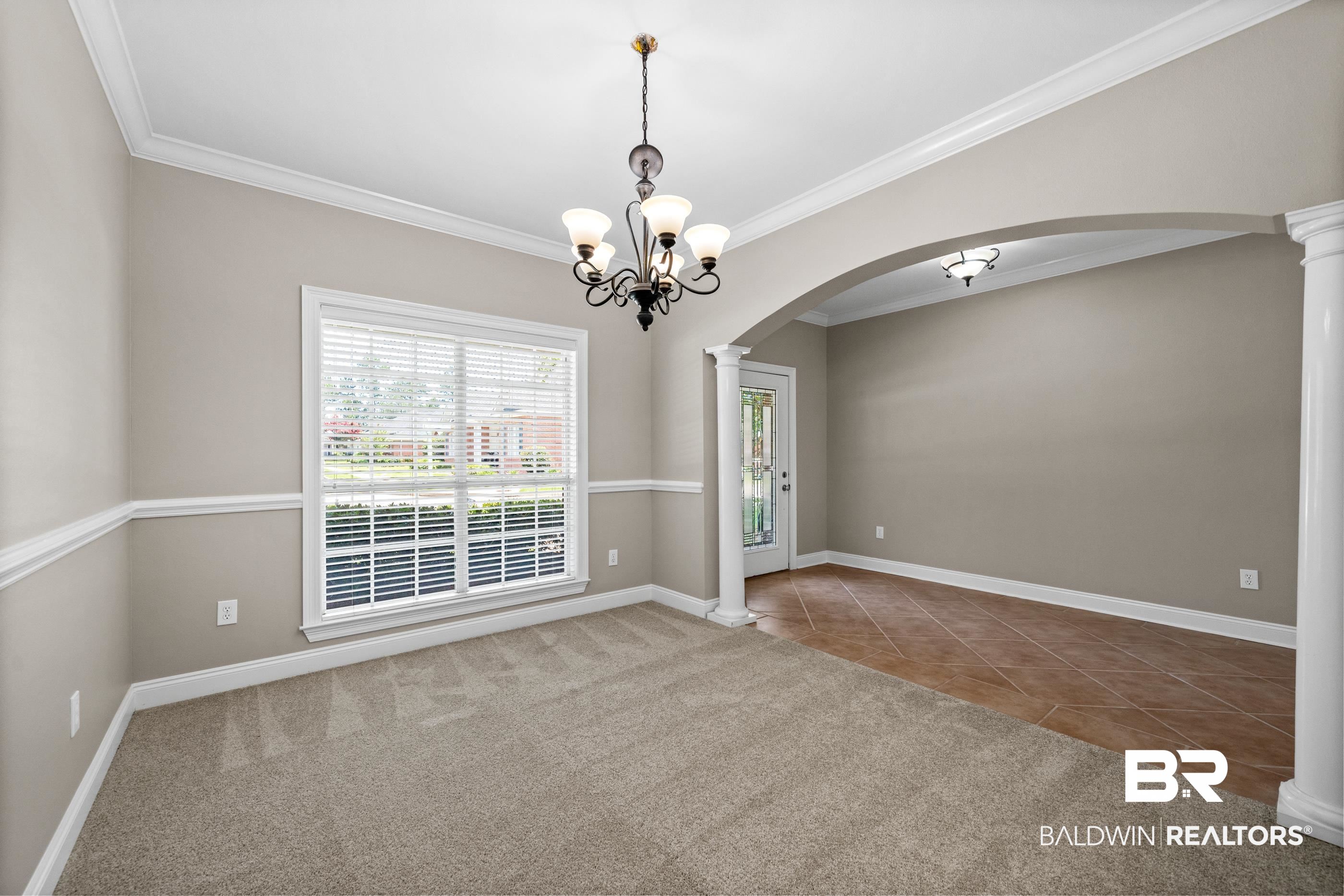 303 Savannah Circle Foley, AL 36535 - Photo 4 of 34 Spacious interior featuring a decorative chandelier, crown molding, chair rail molding, a large window with blinds, and an architectural arched entryway with columns