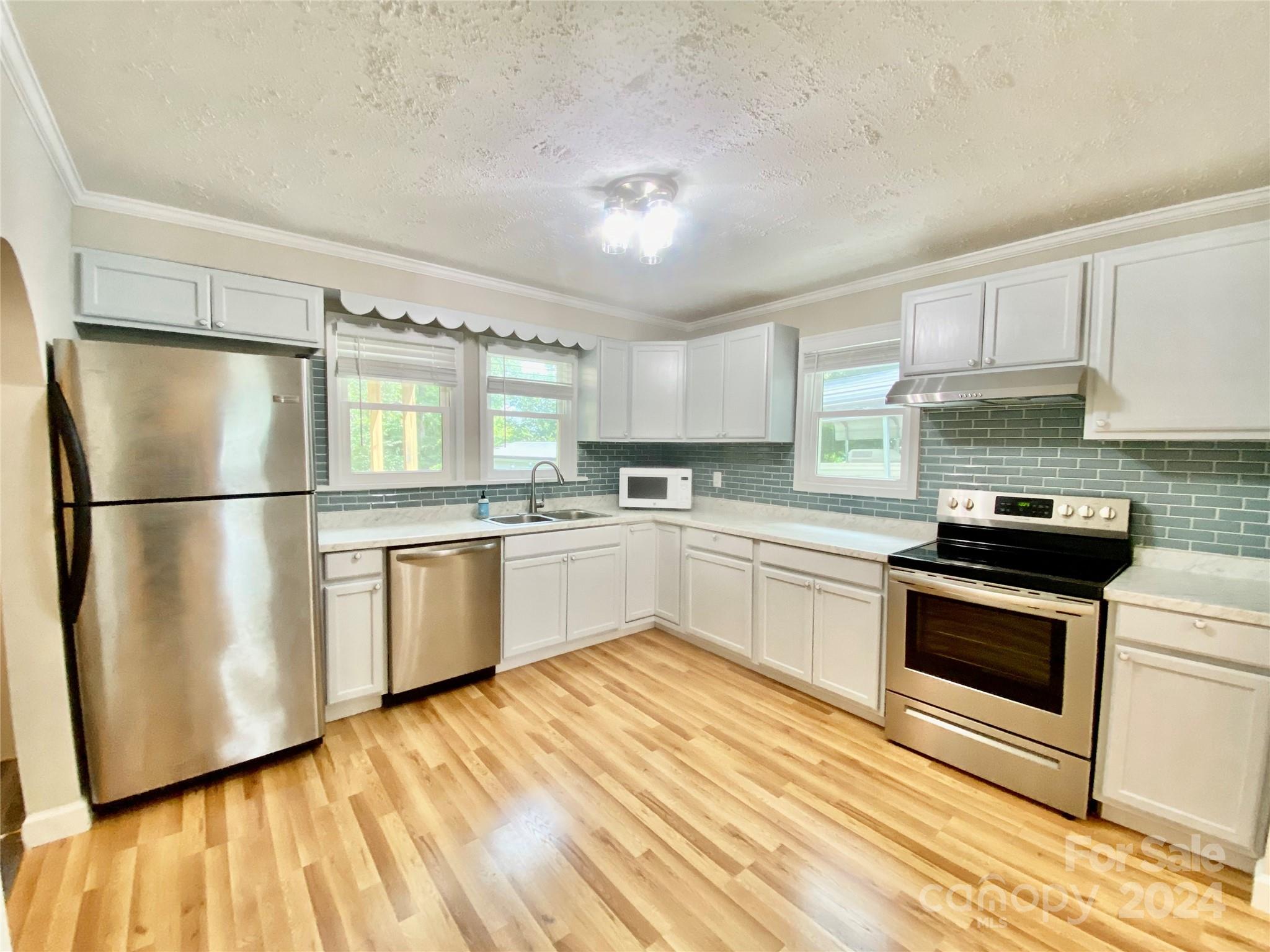 4250 Potneck Road Woodleaf, NC 27054 - Photo 23 of 36 a kitchen with white cabinets stainless steel appliances and wooden floor