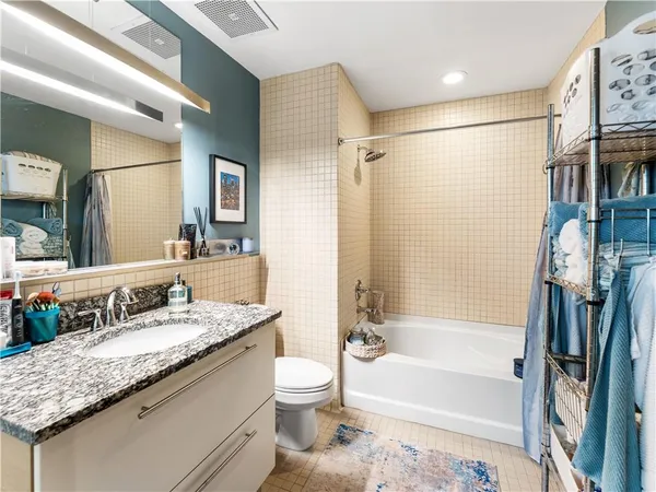 a bathroom with a granite countertop bathtub shower sink vanity and toilet