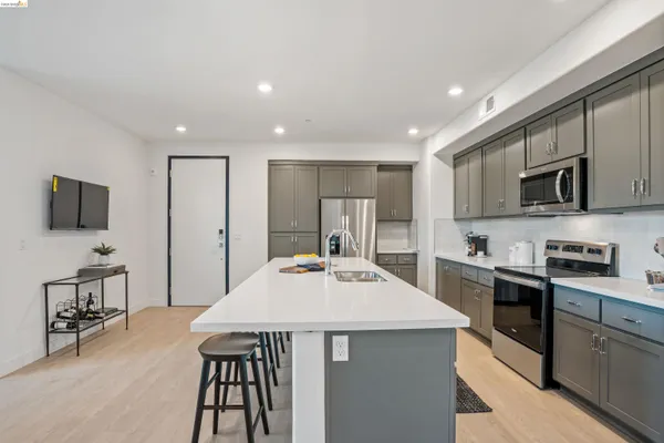 a kitchen with stainless steel appliances a stove a sink a microwave a refrigerator white cabinets and wooden floor