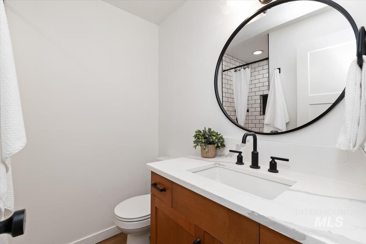 2217 North Middlefield Road Boise, ID 83704 - Photo 24 of 34 Bathroom featuring a wood-finish vanity with a white countertop and integrated sink, matte black faucet, and a large round mirror