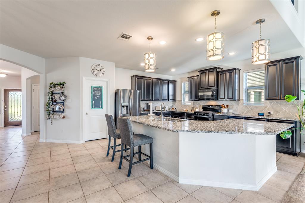 4542 Kipling Avenue Aubrey, TX 76227 - Photo 12 of 36 Kitchen featuring decorative backsplash, arched walkways, a large island with sink, pendant lighting, and a kitchen bar