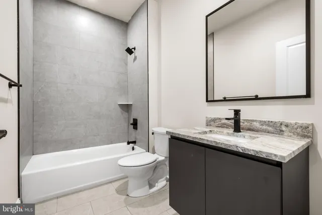 a bathroom with a granite countertop bathtub sink vanity mirror and toilet
