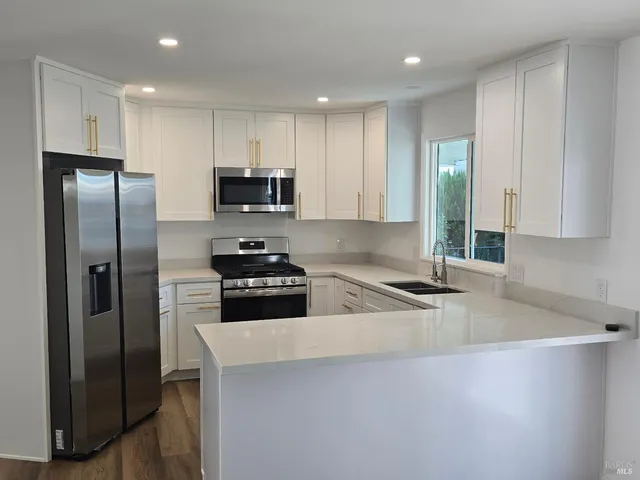 a kitchen with stainless steel appliances granite countertop a refrigerator a stove and a sink with wooden floor