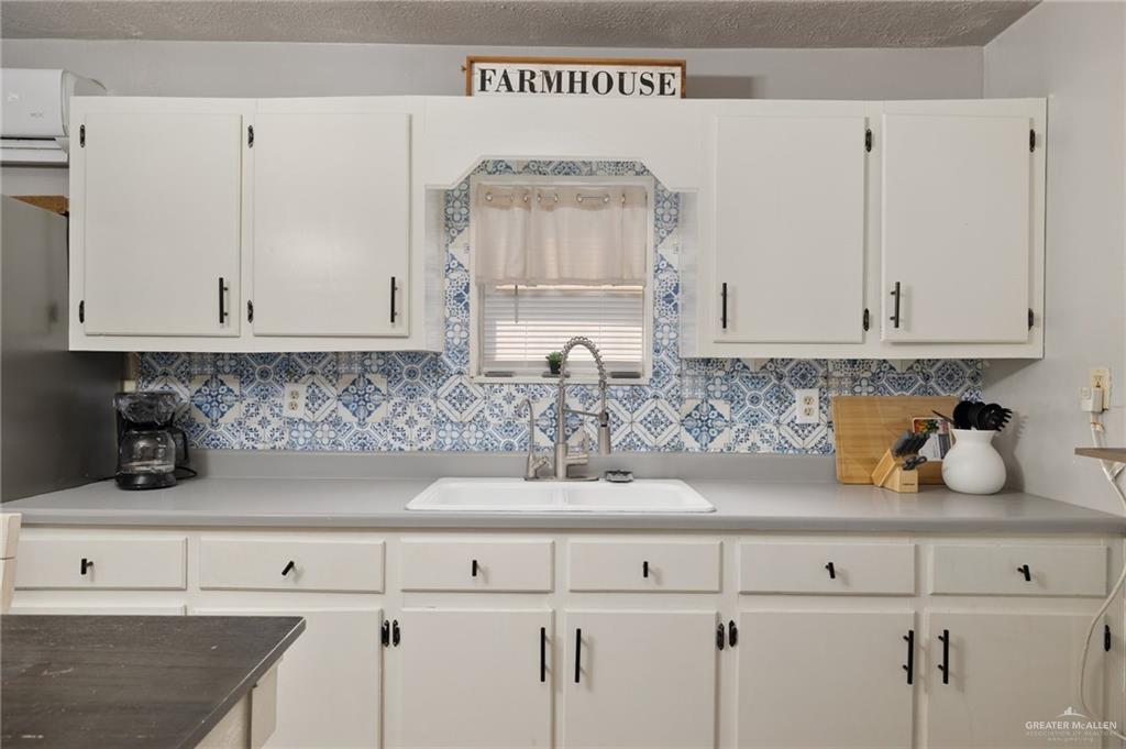 411 East 4th Street Rio Grande City, TX 78582 - Photo 5 of 12 Kitchen featuring white cabinetry with black hardware, a patterned blue and white tile backsplash, a single-basin sink with a gooseneck faucet, and light-toned countertops