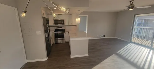 an empty room with wooden floor kitchen microwave and refrigerator