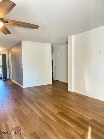 a view of an empty room with wooden floor and a ceiling fan