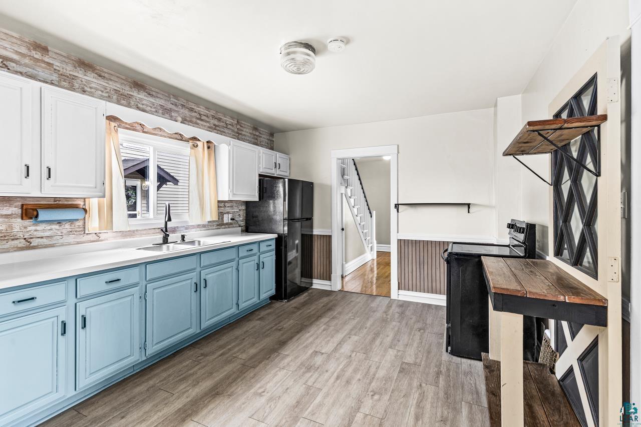 607 3rd Avenue East Superior, WI 54880 - Photo 14 of 41 Dual tone kitchen with two tone cabinetry, black appliances, light countertops, light wood finished floors, and a wainscoted wall