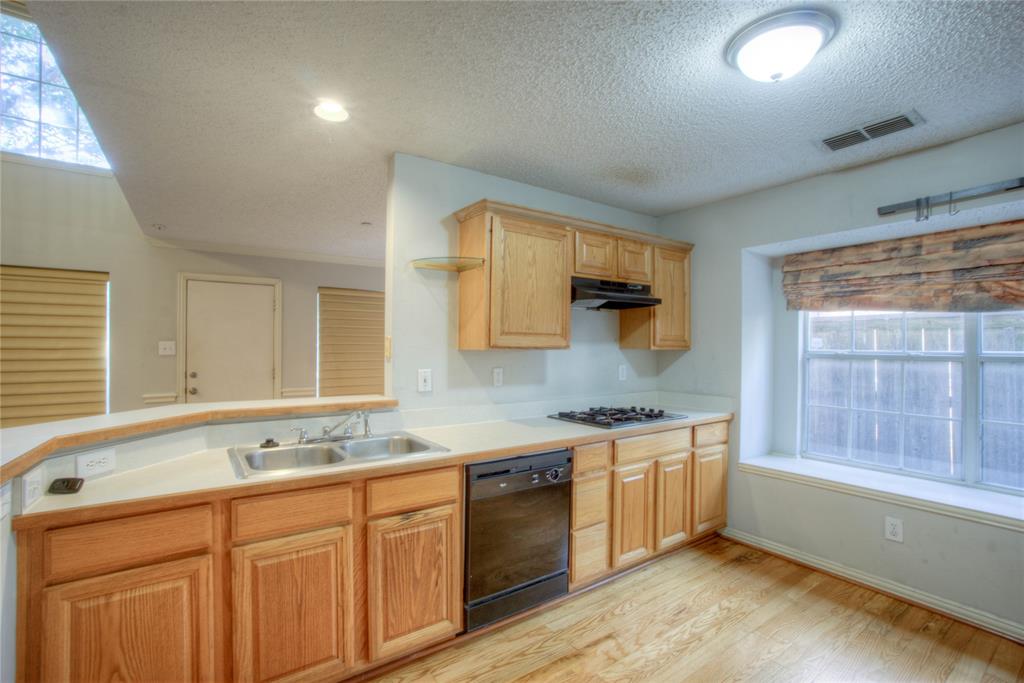 14584 Whitman Court Addison, TX 75001 - Photo 12 of 24 Kitchen featuring black dishwasher, light countertops, a textured ceiling, light wood-type flooring, and light brown cabinetry