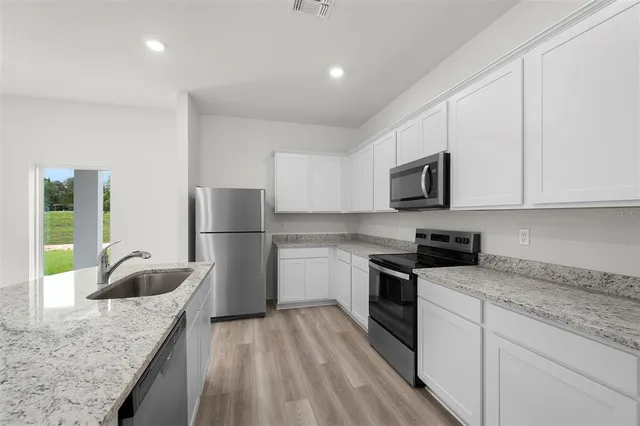 a kitchen with granite countertop a sink a stove top oven a refrigerator and white cabinets