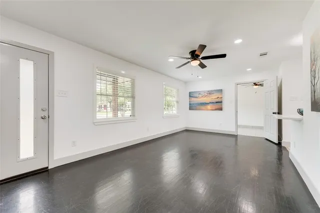an empty room with wooden floor chandelier fan and windows