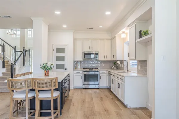 a open kitchen with stainless steel appliances granite countertop a stove top oven a sink dishwasher and white cabinets with wooden floor