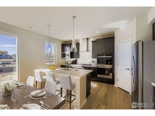 a kitchen with stainless steel appliances kitchen island granite countertop a refrigerator a stove a sink a dining table and chairs with wooden floor