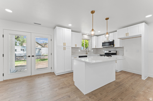 1898 West 600 South Provo, UT 84601 - Photo 5 of 32 Modern kitchen featuring an island with a light-toned countertop, white cabinetry with gold-toned hardware, and stainless steel appliances
