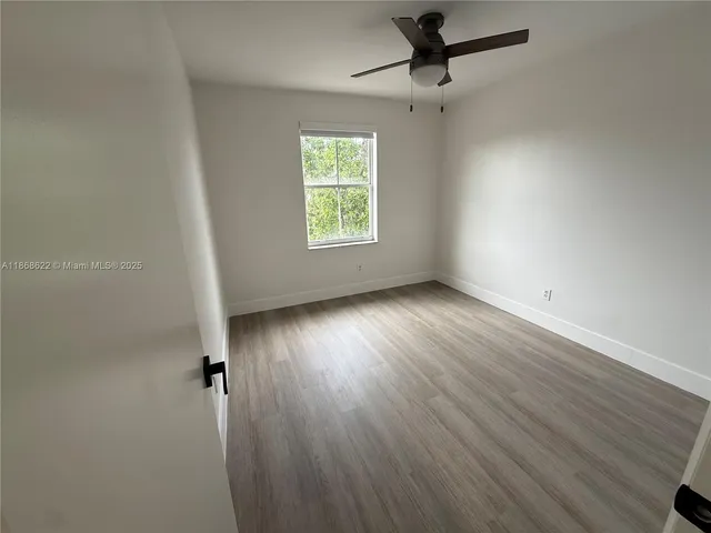 an empty room with wooden floor fan and windows