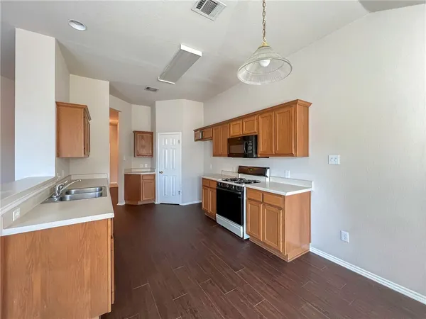 a kitchen with stainless steel appliances a stove top oven a sink dishwasher and a refrigerator with wooden floor