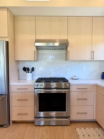 a stove top oven sitting inside of a kitchen with stainless steel appliances wooden floor and a sink