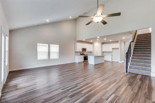 a view of an empty room with wooden floor and a ceiling fan